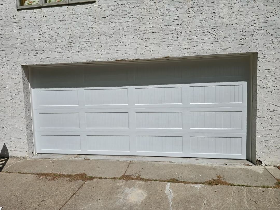White garage door set into a stucco wall with a concrete driveway in front