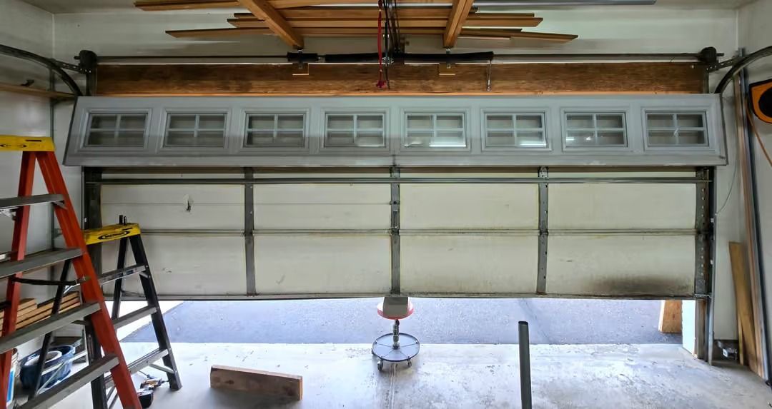 Open garage door with a ladder on the left and a hanging light fixture in the center