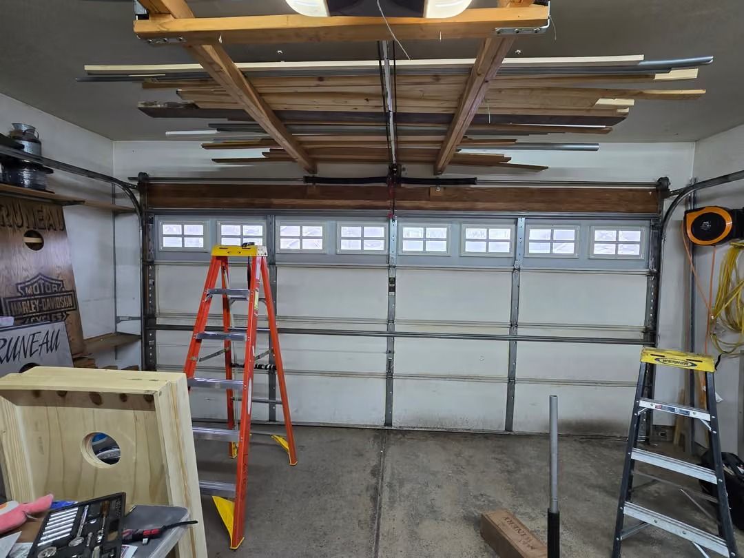 Garage under construction with a red ladder, open ceiling framing, and a closed white garage door.
