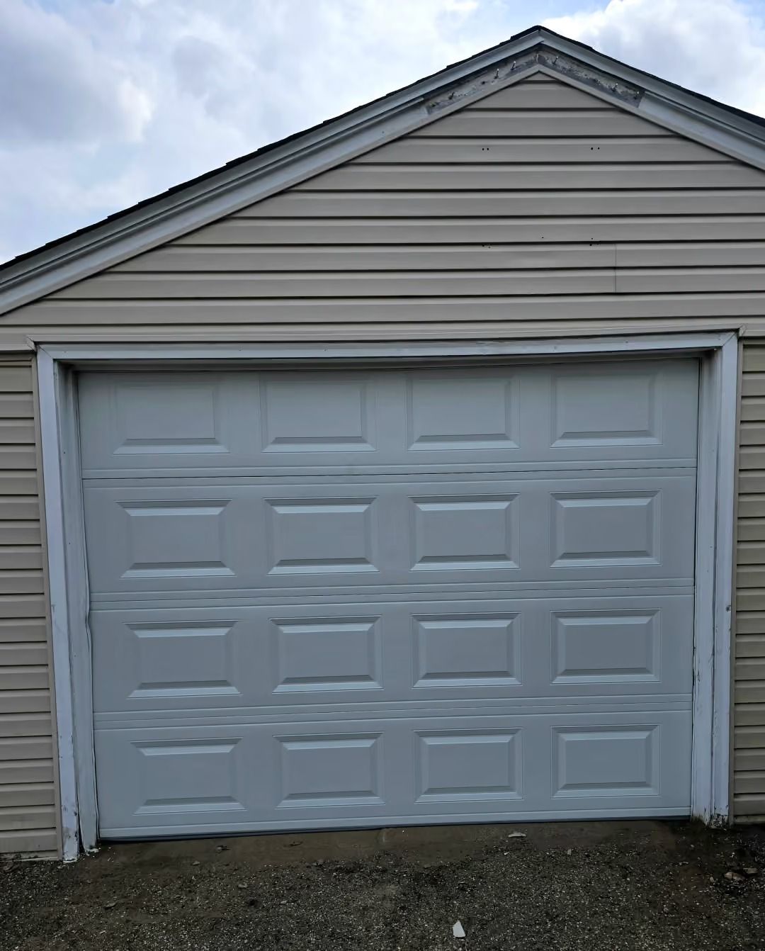 Small white garage with closed paneled door and gray siding under a gabled roof