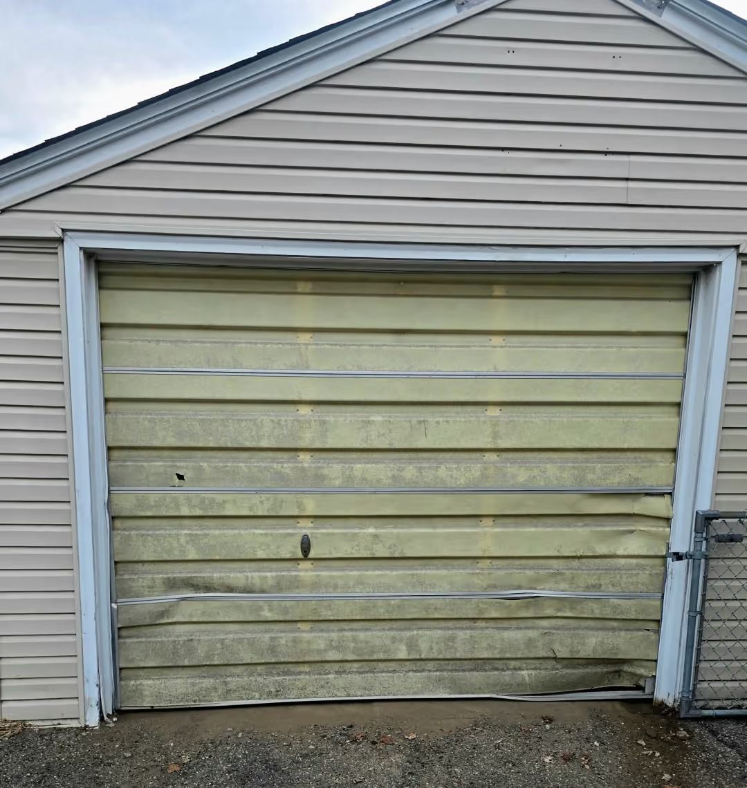 Old beige garage door with peeling paint on a house exterior