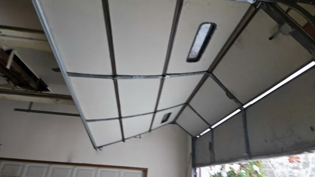 Damaged garage door panel bent inward, exposing the frame and ceiling