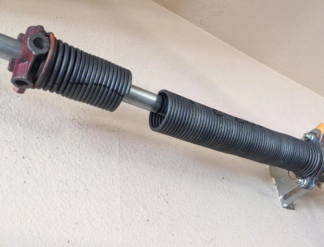 Close-up of a black garage door torsion spring and shaft mounted near a ceiling