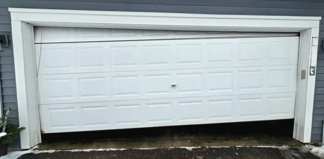 White garage door on a house with a small dark dent near the center and wet pavement below