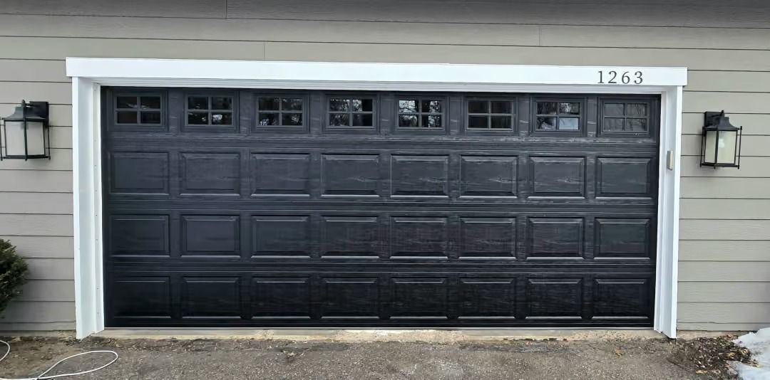Dark gray two-car garage door with white trim and wall lanterns