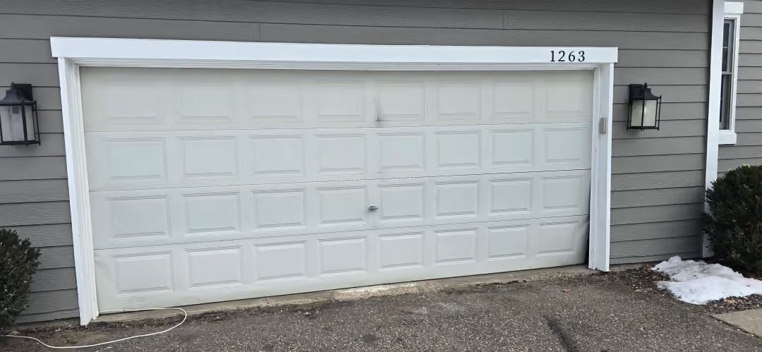 White double garage door on a gray house exterior with a small patch of snow nearby