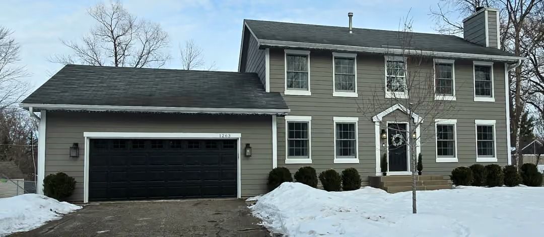 Snowy suburban house with attached garage and brick-and-siding exterior