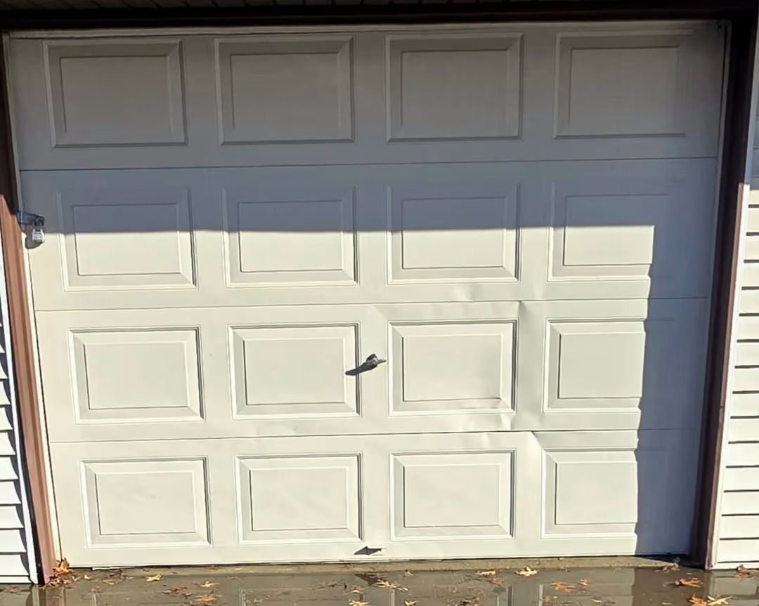 White paneled garage door with a small dent in the center, viewed in daylight.