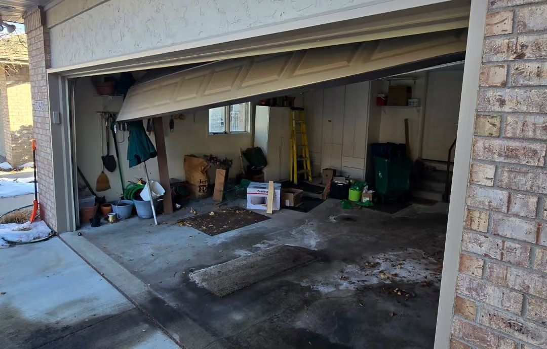 Partially open garage with tools, storage items, and concrete floor, viewed from the driveway