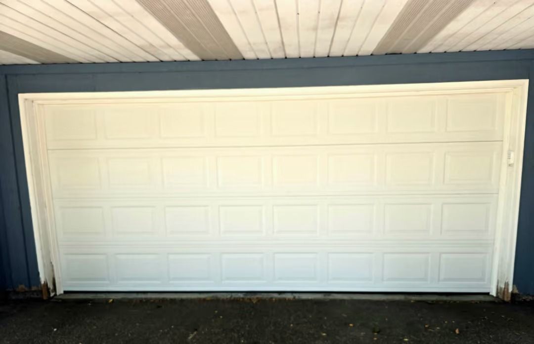 White garage door on a blue building exterior with a covered ceiling above.