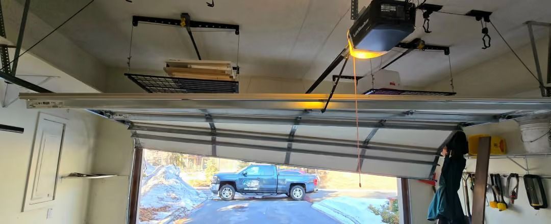 Inside a garage, an open door reveals a blue SUV parked in a snowy driveway.