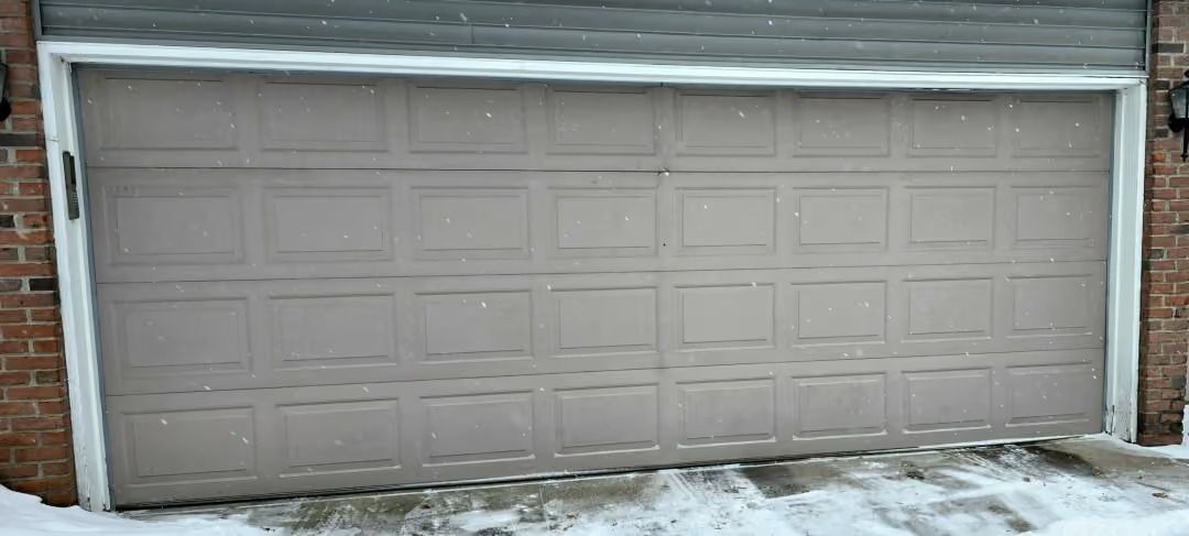 Snow-covered garage door on a house with brick siding and a snowy driveway