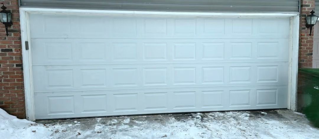 White garage door on a brick building with snow on the ground