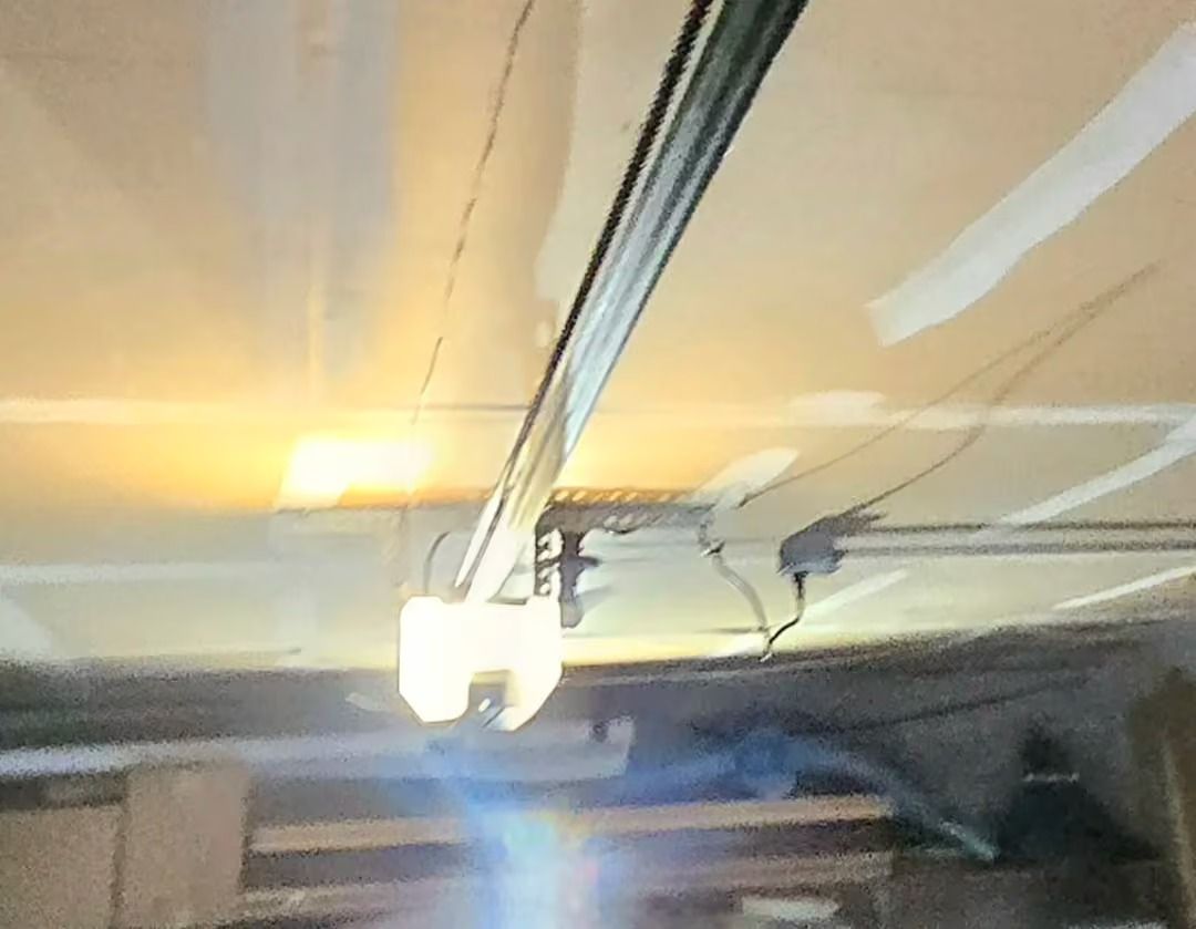 Ceiling-mounted garage door opener with tracks and wiring overhead.