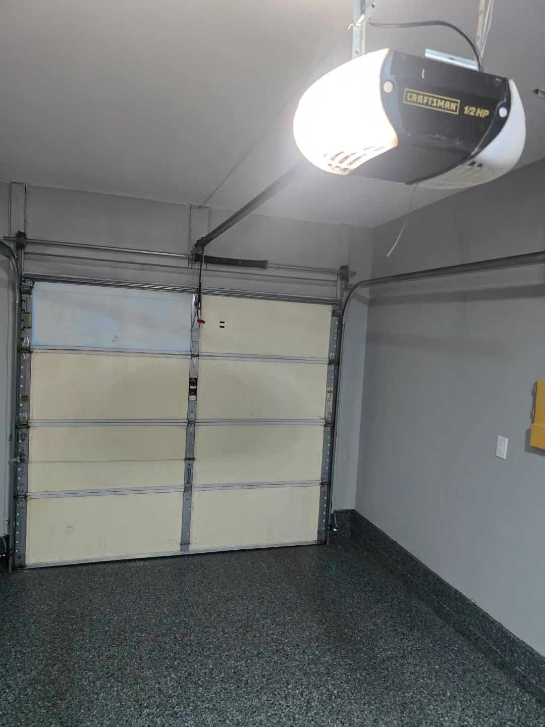 Empty garage interior with closed sectional door, gray walls, and overhead garage door opener