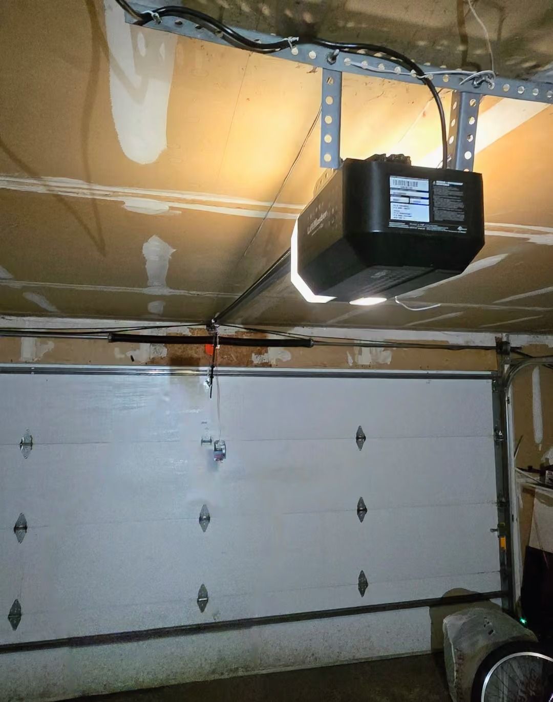 Garage door with a black opener mounted on the ceiling and exposed insulation overhead.