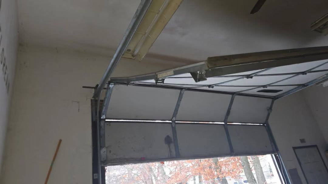 Open garage door partially raised, showing interior ceiling and a snowy or bright outdoor view.