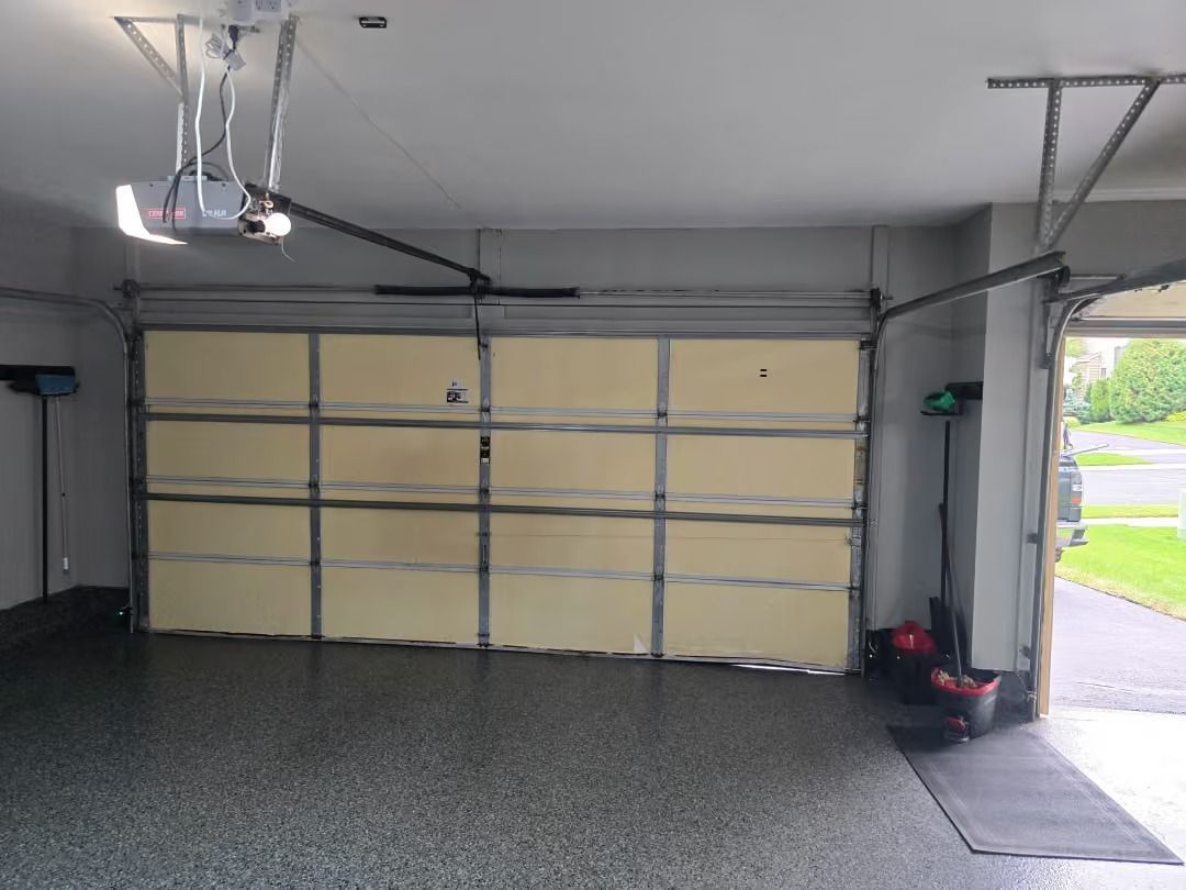 Empty garage interior with closed beige sectional door and open side entry to driveway.