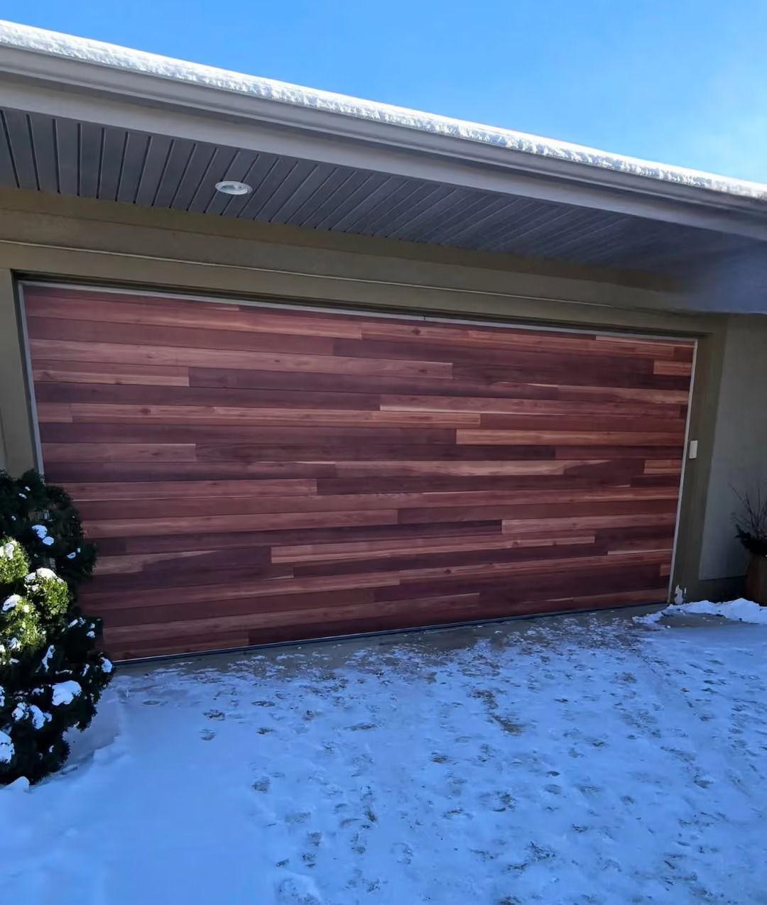 Closed wood-paneled garage door on a house with snow on the ground under a blue sky