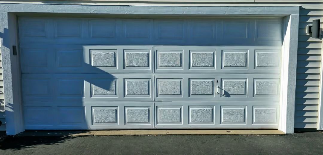 White two-car garage door with blue trim and a shadow on the left side.