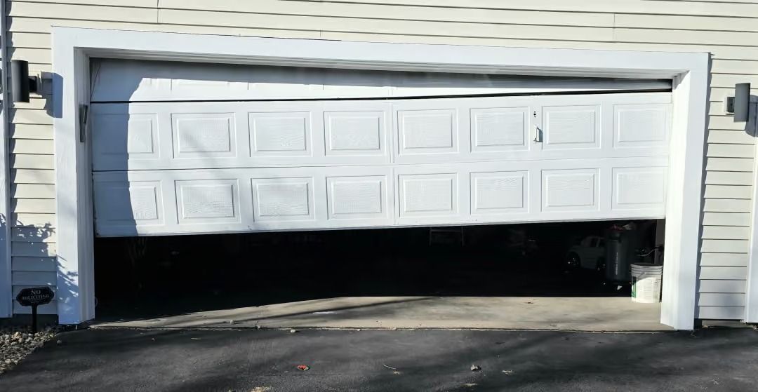 Partially open white garage door with black interior shadow and daylight outside