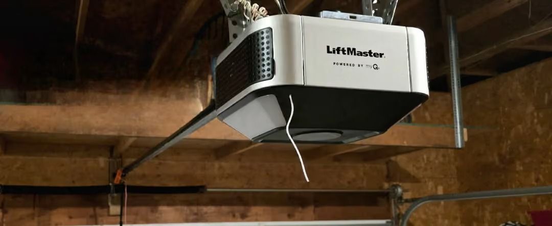 White garage door opener mounted to a wooden ceiling with hanging pull cords and wires