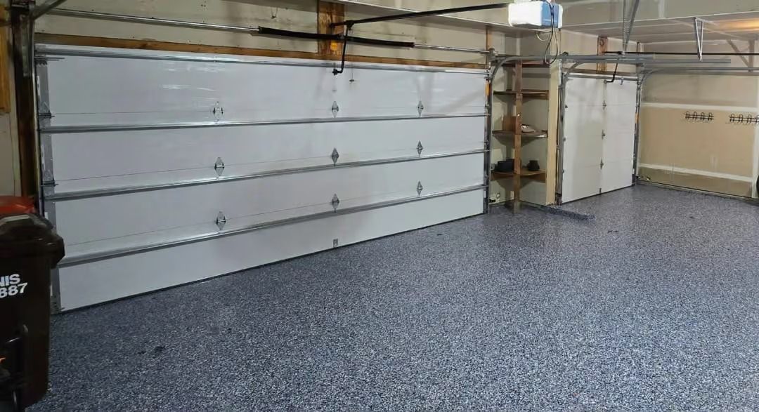 Empty garage with closed white cabinets along the wall and a speckled gray floor