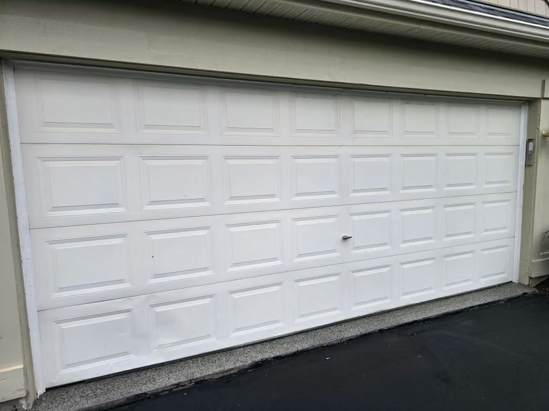 White double garage door on a beige house with a dark driveway in front.