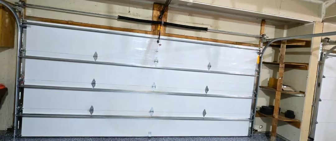 White garage door with horizontal panels and a wooden shelf unit on the right side of a workshop wall.