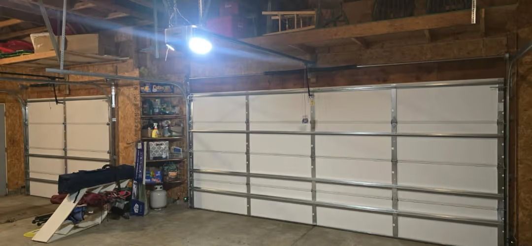 Garage interior with a large white roll-up door, tools, and a bright overhead light