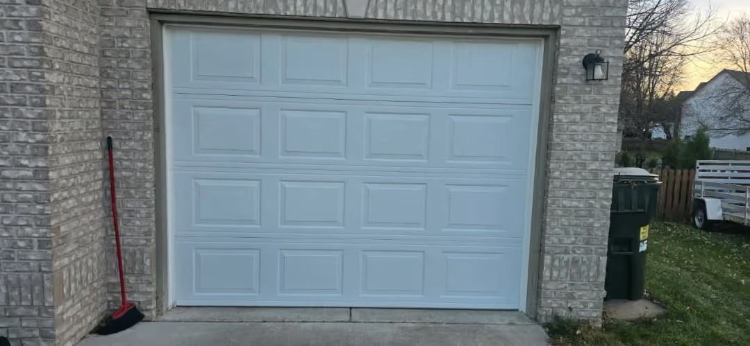 White garage door on a stone house with a broom and black mat beside it