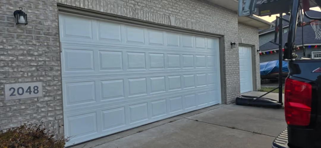 White double garage door on a stone house with the number 2048 beside it, next to a parked vehicle.