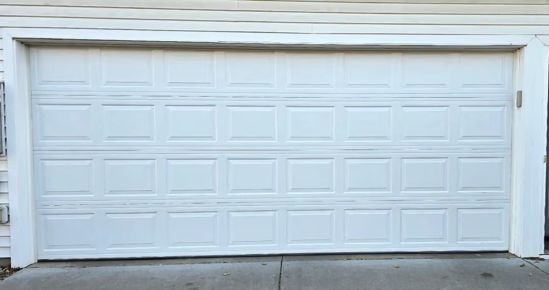 White garage door on a house exterior with a concrete driveway and light siding