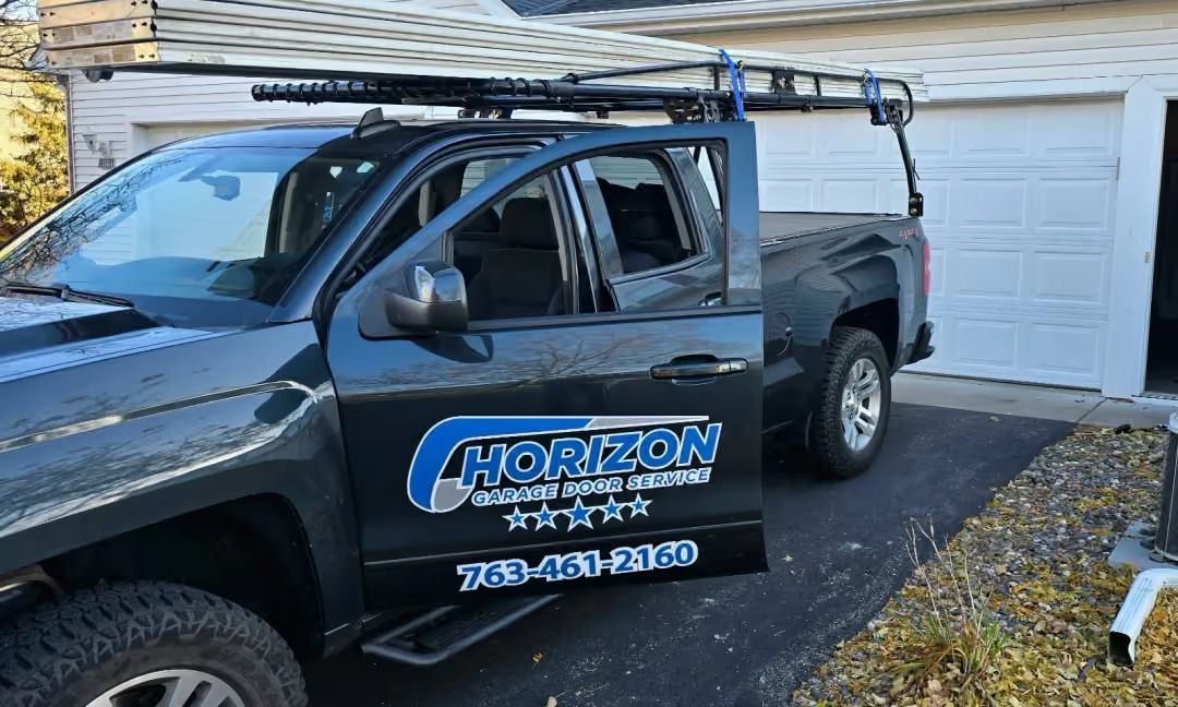 Black work truck with Horizon signage parked in front of a garage, carrying roof-mounted equipment.