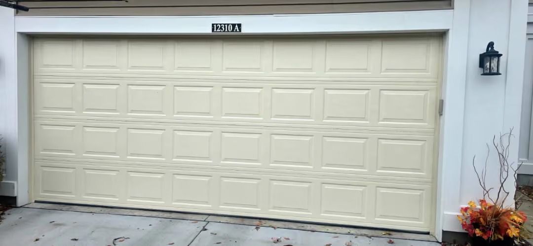 Cream-colored double garage door on a house exterior with a small porch light and autumn flowers.