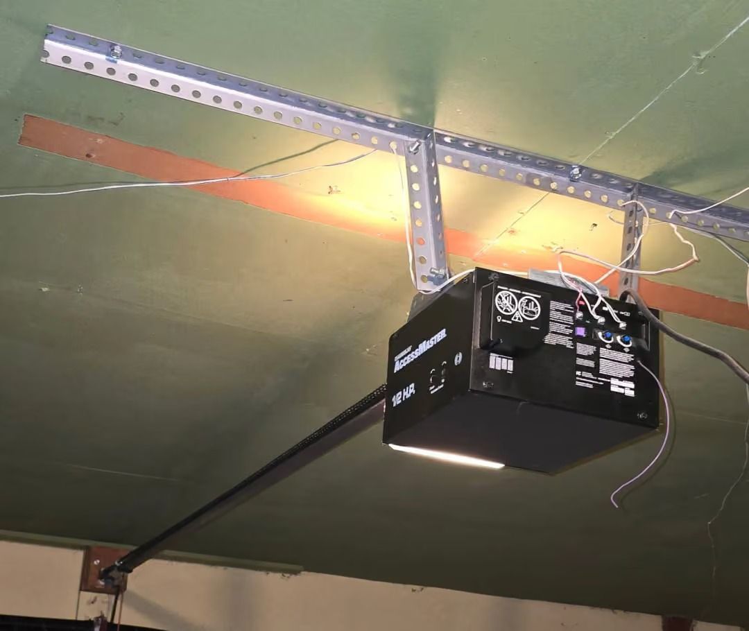 Ceiling-mounted garage door opener with chain rail and hanging wires on a green ceiling.