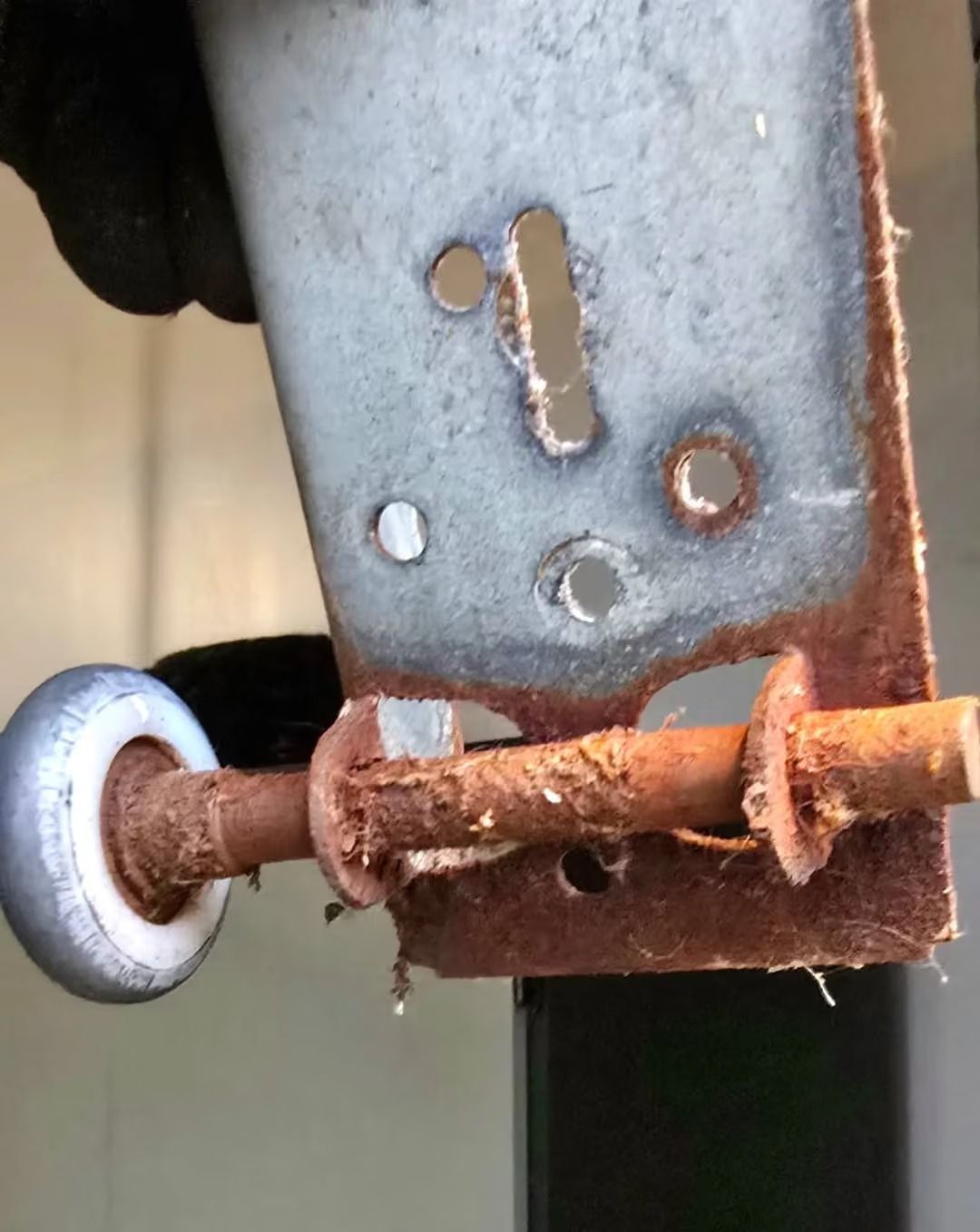 Rusty metal latch with worn bolt and wheel on a weathered gray frame