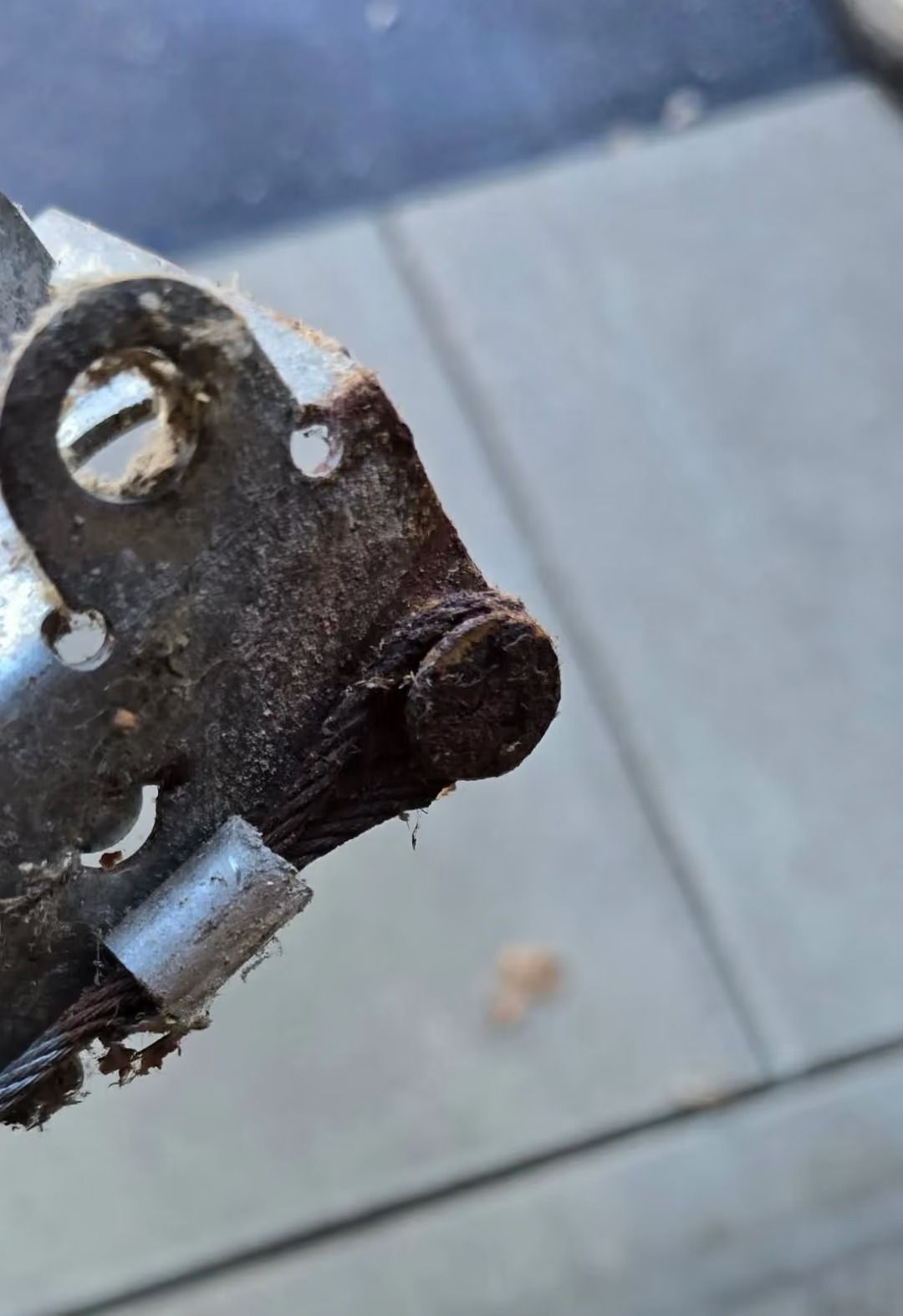 Close-up of a rusted metal tool part with a circular hole on a sidewalk background