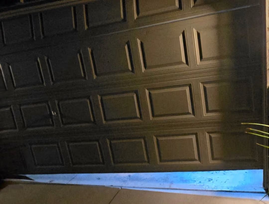Partially opened black garage door with a blue strip of light at the bottom