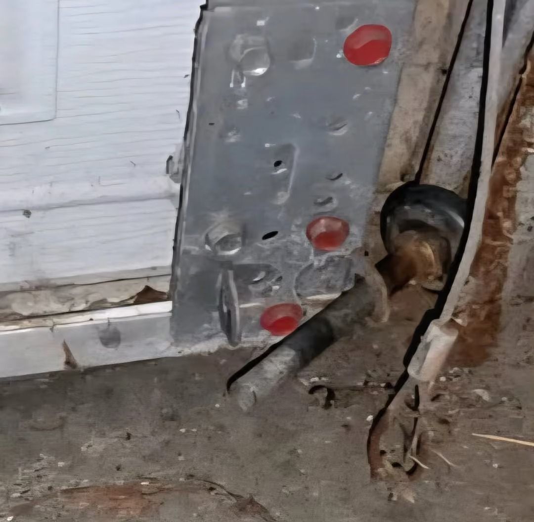 Gray metal plate with red plugs beside a wall and floor, with exposed cable or pipe at the base.