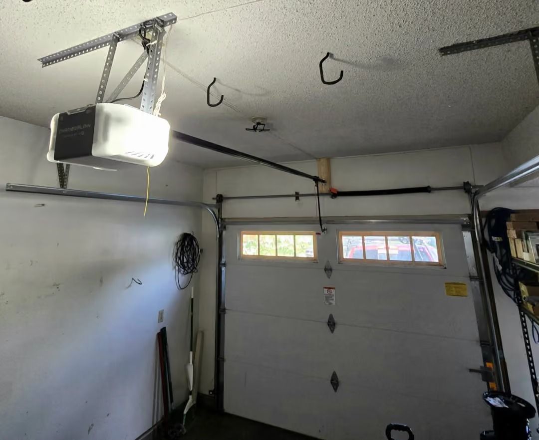 Garage interior with an overhead door opener, hanging hooks, and storage items on the walls.