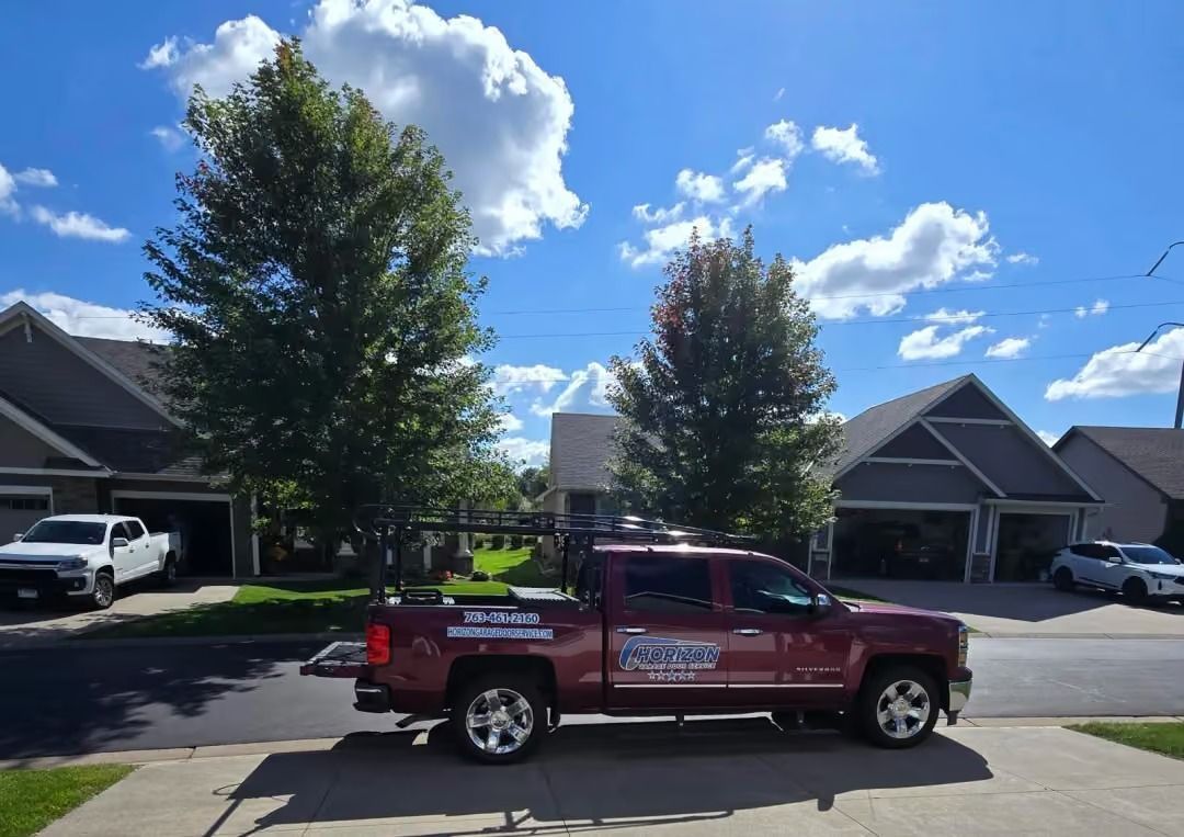 Red pickup truck parked on a suburban street with houses and tall trees under a bright blue sky.
