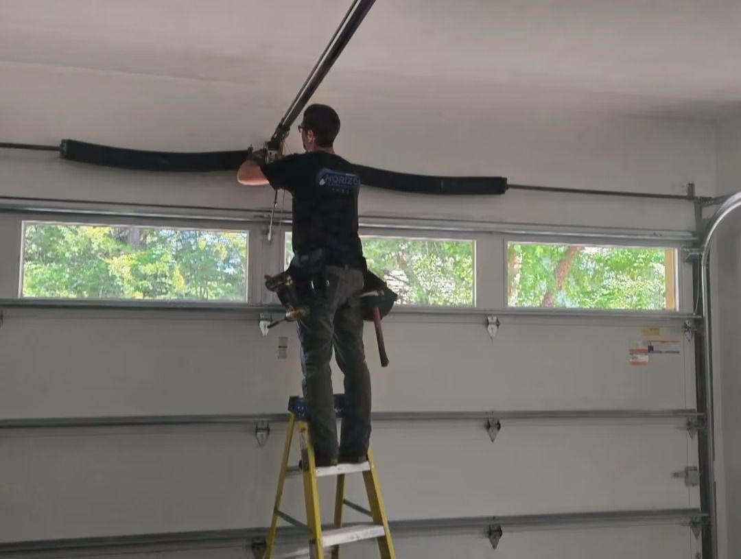 Person on a ladder installing a garage door opener track in a garage