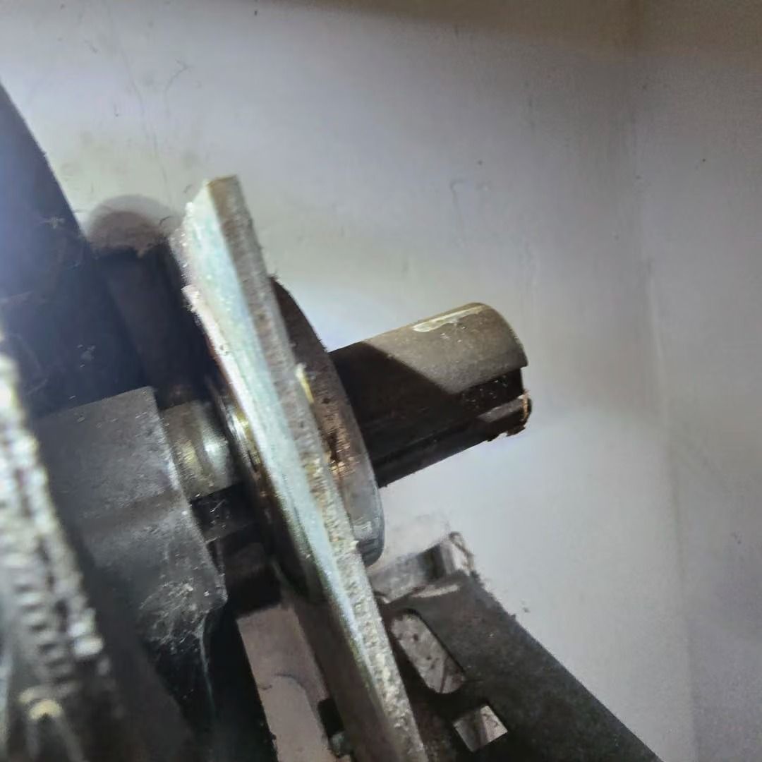 Close-up of a metal shaft and circular plate on a mechanical assembly, viewed from the side.