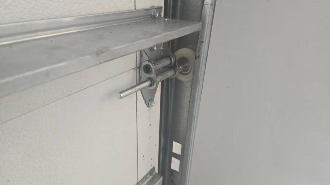 Close-up of a metal shelf bracket and screws mounted on a light gray wall panel.