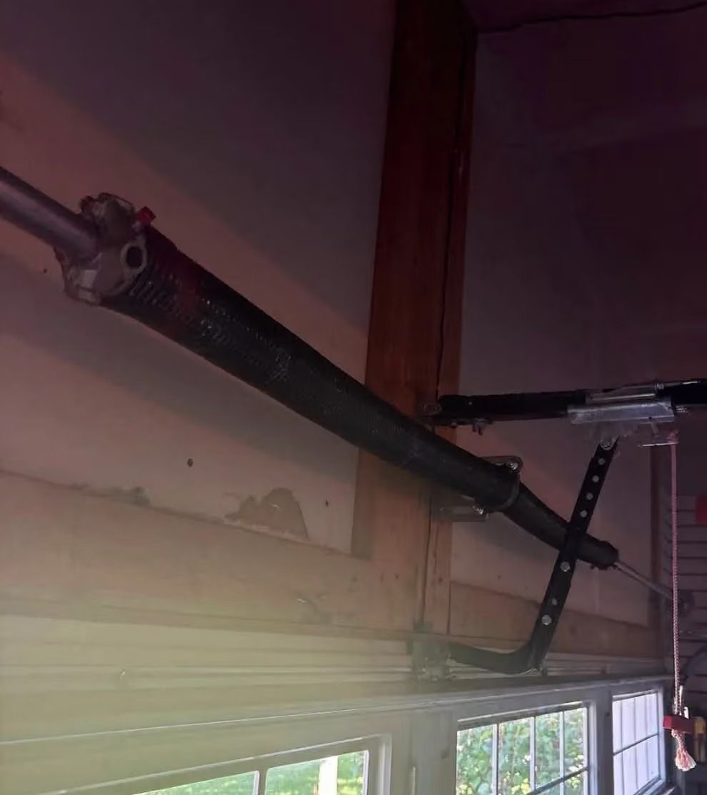 Black pipe or duct runs along a ceiling above a window in a dim room.