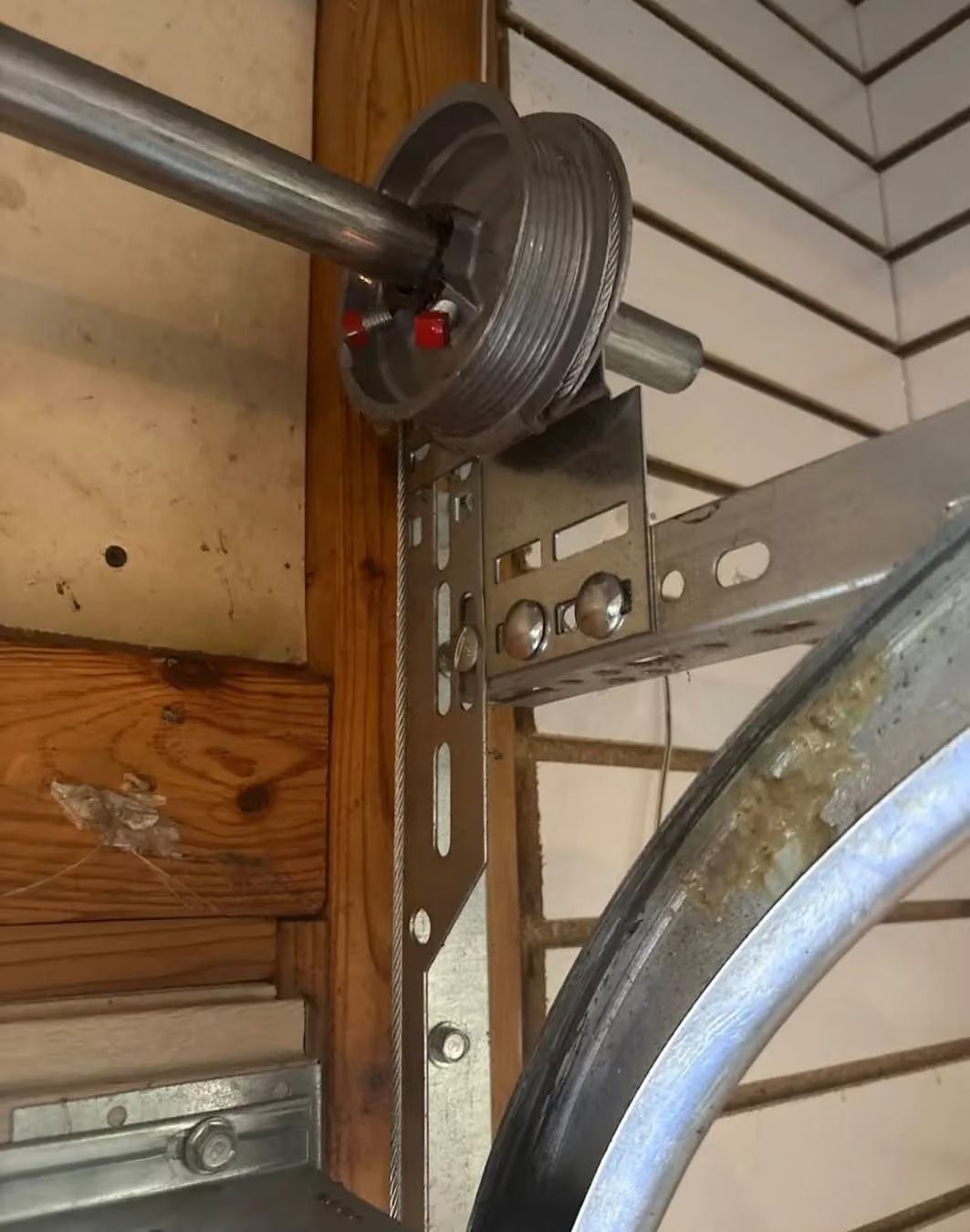 Garage door opener bracket and pulley assembly mounted on a wall near a wooden beam.