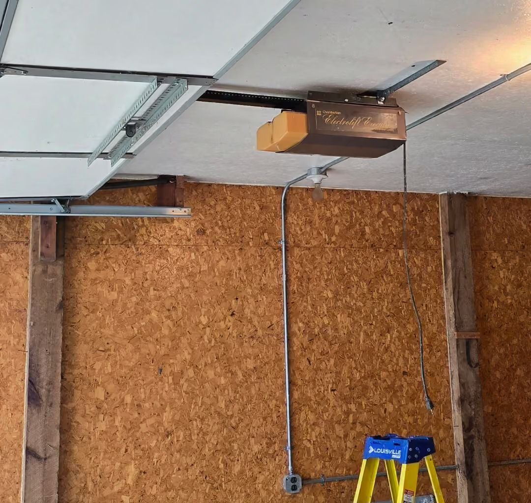 Garage ceiling with an overhead door opener, wood panel wall, and a yellow ladder below.