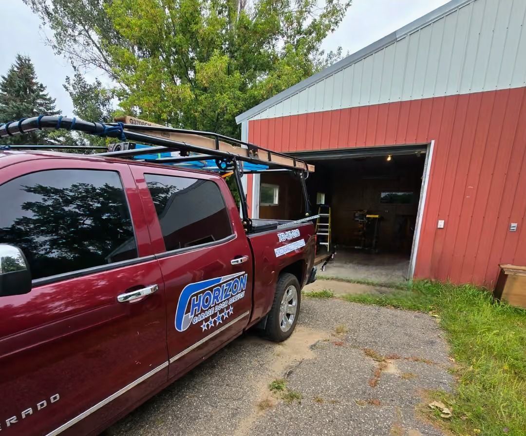 Red service truck parked beside an open garage in a red barn-like building.