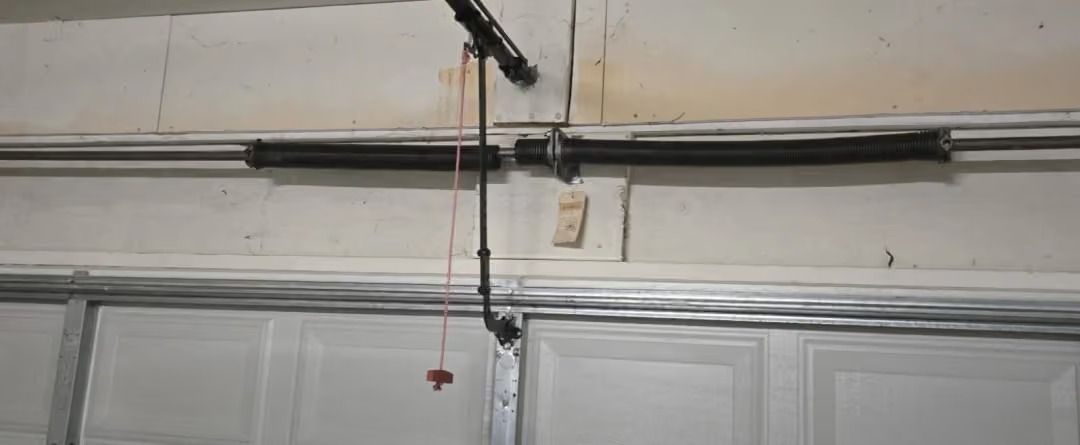 Garage ceiling with exposed pipes, hanging cords, and a small pull chain above a white door panel